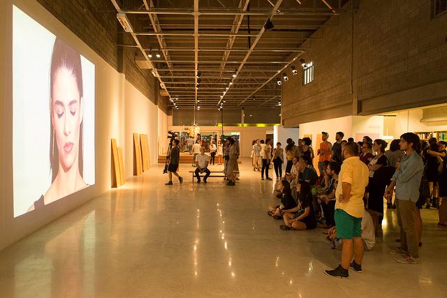 P&uacute;blico assiste um dos v&iacute;deos da exposi&ccedil;&atilde;o na noite de abertura do galp&atilde;o