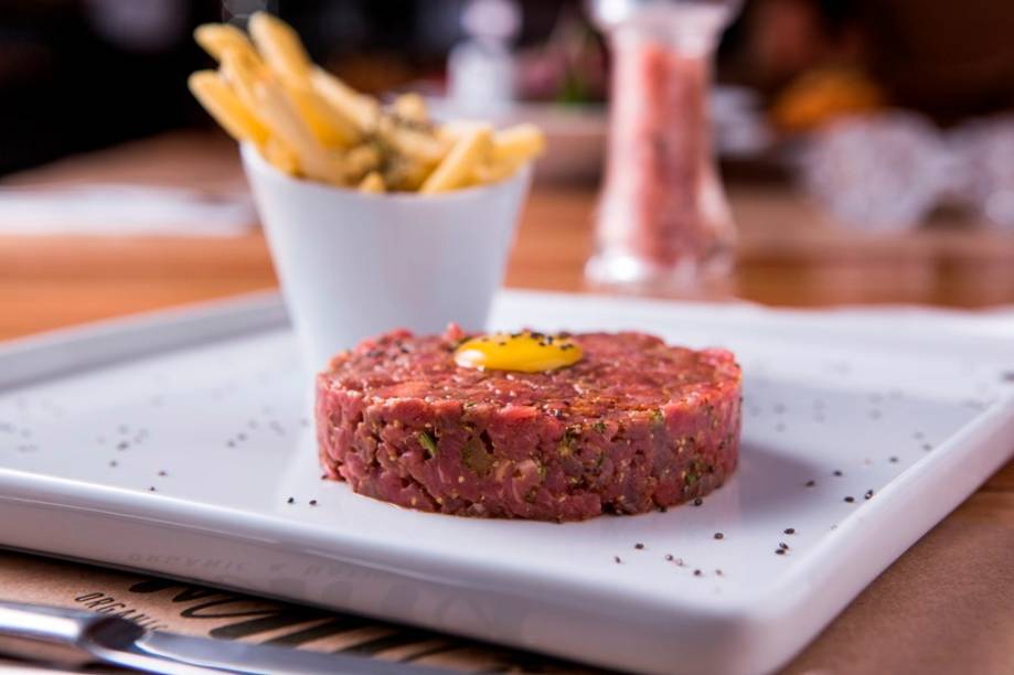 Coberto por uma gema ovo de codorna, o steak tartare chega junto de batata frita ao alecrim