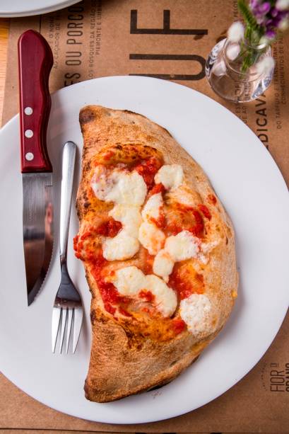 Fechado como um pastelão, o calzone leva recheio de presunto, mussarela, tomate e creme de alcachofra Fechado como um pastelão, o calzone leva recheio de presunto, mussarela, tomate e creme de alcachofra