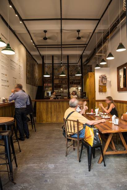 O pequeno salão com lugares se divide entre um balcão lateral e a mesa comunitária O pequeno salão com lugares se divide entre um balcão lateral e a mesa comunitária