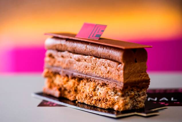 Montado sob uma base de avelã, o plaisir du chocolat intercala crocante de praliné, ganache, folhas e chantili de chocolate Montado sob uma base de avelã, o plaisir du chocolat intercala crocante de praliné, ganache, folhas e chantili de chocolate