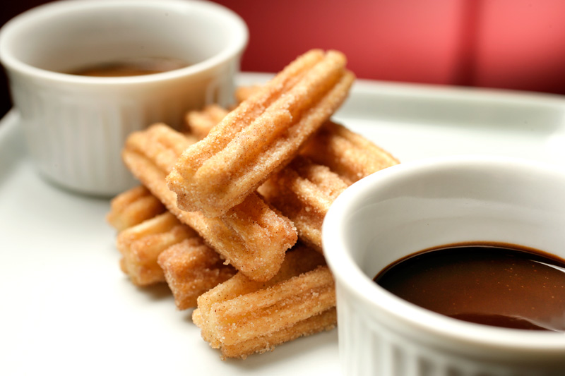 A porção de churros vem à mesa com doce de leite ou chocolate