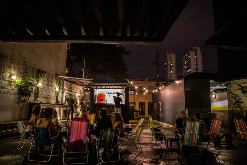 Cordões com lâmpadas penduradas, cadeiras praianas e mesas de ripa compõe o cenário Cordões com lâmpadas penduradas, cadeiras praianas e mesas de ripa compõe o cenário