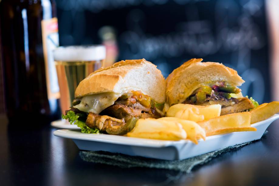 O sanduba de pernil de estádio vem todo ajeitado no prato junto de fritas O sanduba de pernil de estádio vem todo ajeitado no prato junto de fritas
