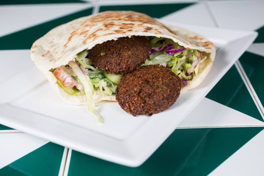 Enrolado no pão pita, o sanduba de faláfel junta alface, tomate, repolho, cebola-roxa, pepino em conserva e molho tahine Enrolado no pão pita, o sanduba de faláfel junta alface, tomate, repolho, cebola-roxa, pepino em conserva e molho tahine