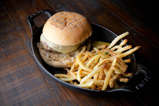 Ici Brasserie: hambúrguer com cebola caramelada e queijo emmental ladeado por fritas Ici Brasserie: hambúrguer com cebola caramelada e queijo emmental ladeado por fritas