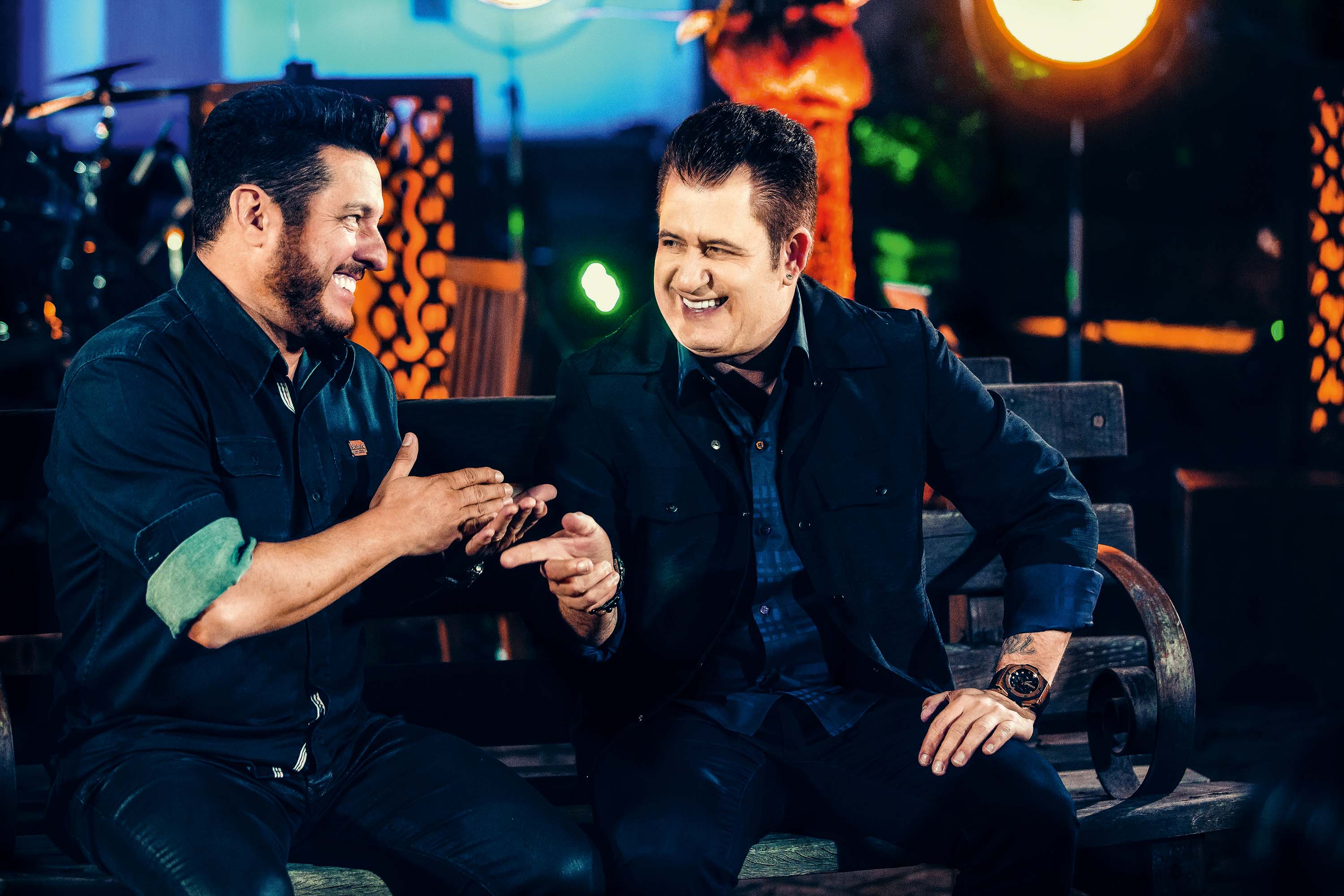 Dois cantores sertanejos sentados no palco