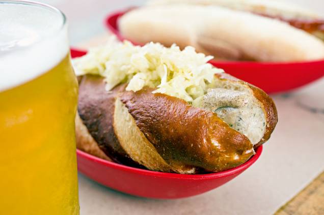 Cachorro-quente com salsicha bratwurst, mostarda escura e chucrute: pão de massa de pretzel Cachorro-quente com salsicha bratwurst, mostarda escura e chucrute: pão de massa de pretzel