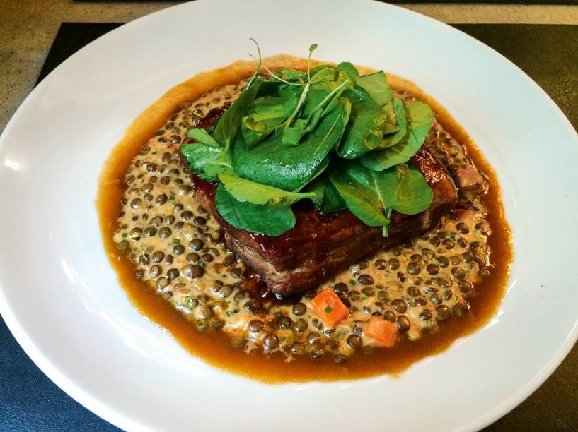 Costelinha de porco assada, coberta por agrião, vem sobre um cozido de lentilha francesa de Puy com um toque de creme de leite Costelinha de porco assada, coberta por agrião, vem sobre um cozido de lentilha francesa de Puy com um toque de creme de leite