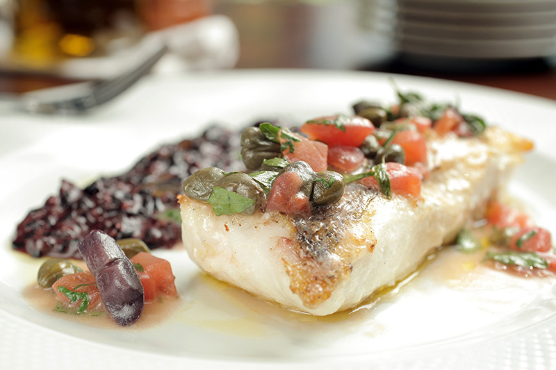 Merluza à siciliana com molho de tomate e alcaparra, acompanhada de risoto de arroz negro Merluza à siciliana com molho de tomate e alcaparra, acompanhada de risoto de arroz negro