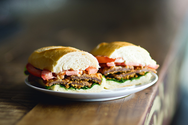 Baguete recheada de duas fatias fininhas de coxão mole à milanesa, vem ainda com maionese de alho, folhas de rúcula e fatias de tomate