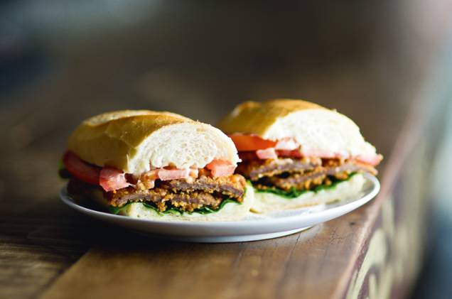 Baguete recheada de duas fatias fininhas de coxão mole à milanesa, vem ainda com maionese de alho, folhas de rúcula e fatias de tomate Baguete recheada de duas fatias fininhas de coxão mole à milanesa, vem ainda com maionese de alho, folhas de rúcula e fatias de tomate