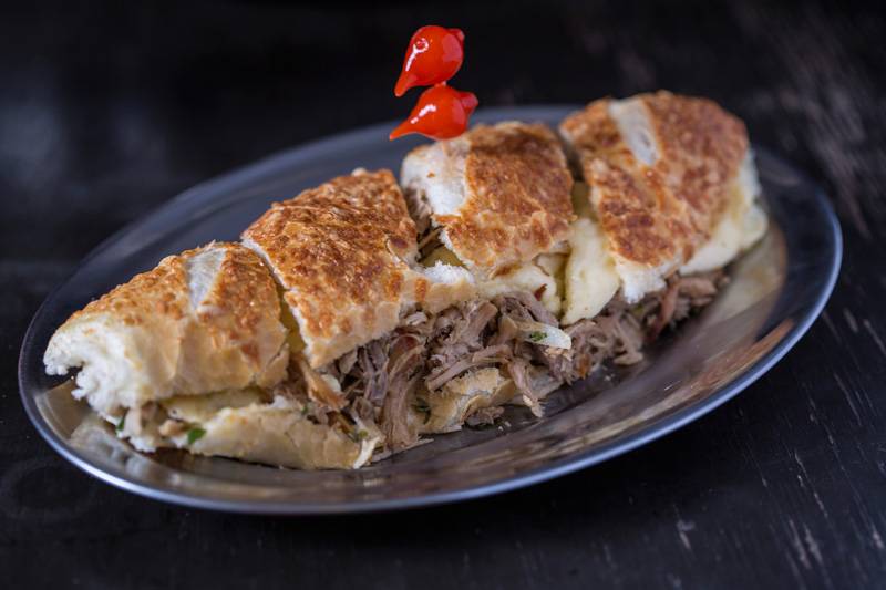 O sanduíche de pernil em lascas, queijo da Serra da Canastra, vinagrete e rúcula na baguete O sanduíche de pernil em lascas, queijo da Serra da Canastra, vinagrete e rúcula na baguete