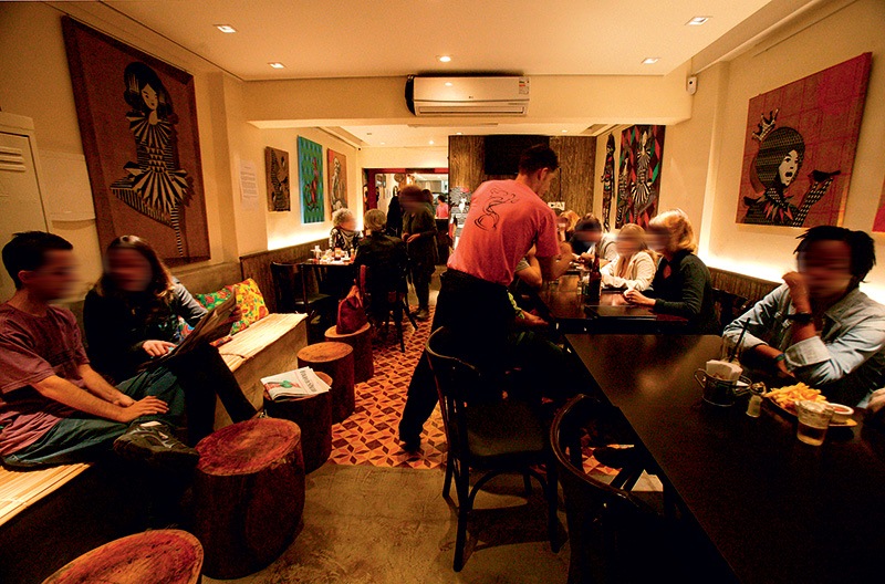 O ambiente: exposição de quadros e sofá com almofadas de chita O ambiente: exposição de quadros e sofá com almofadas de chita