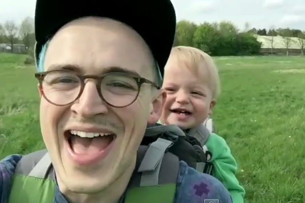 Garotinho ri deliciosamente com seu pai em brincadeira de assoprar um dente-de-leão