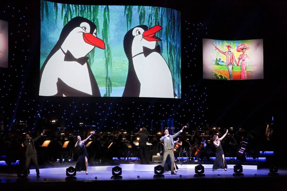 Ao fundo do palco, cenas das películas são reproduzidas em um telão