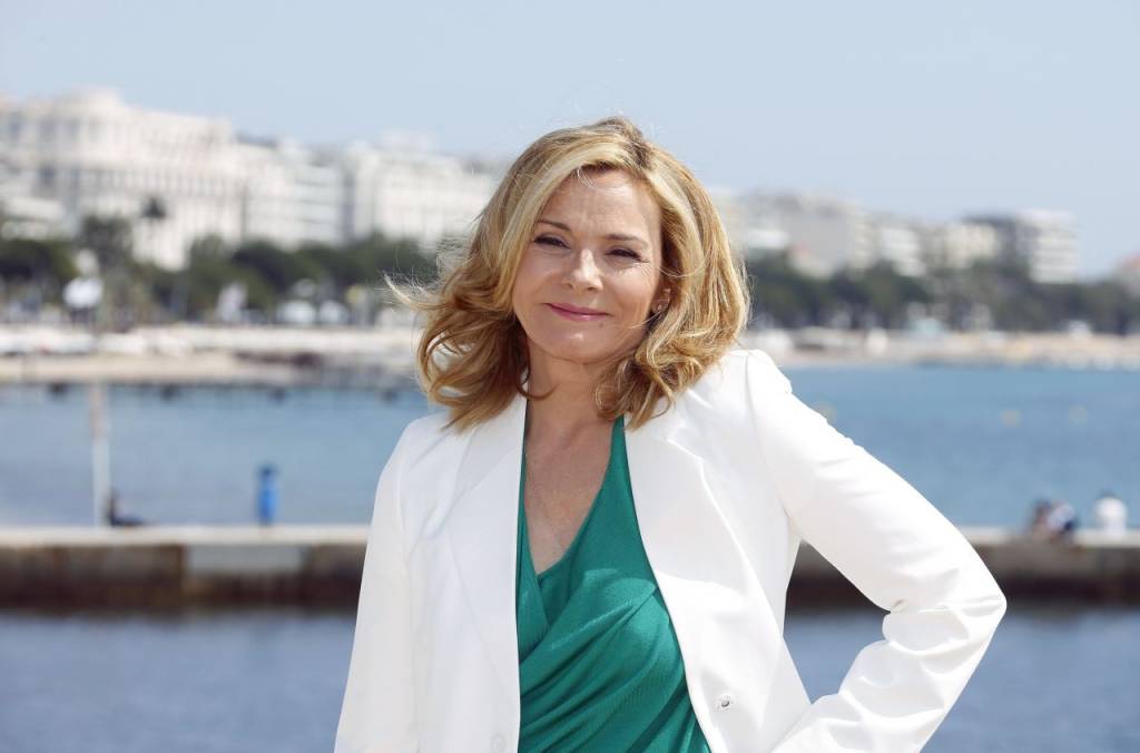 Kim Cattrall posa em frente ao mar com camiseta verde e blazer branco.