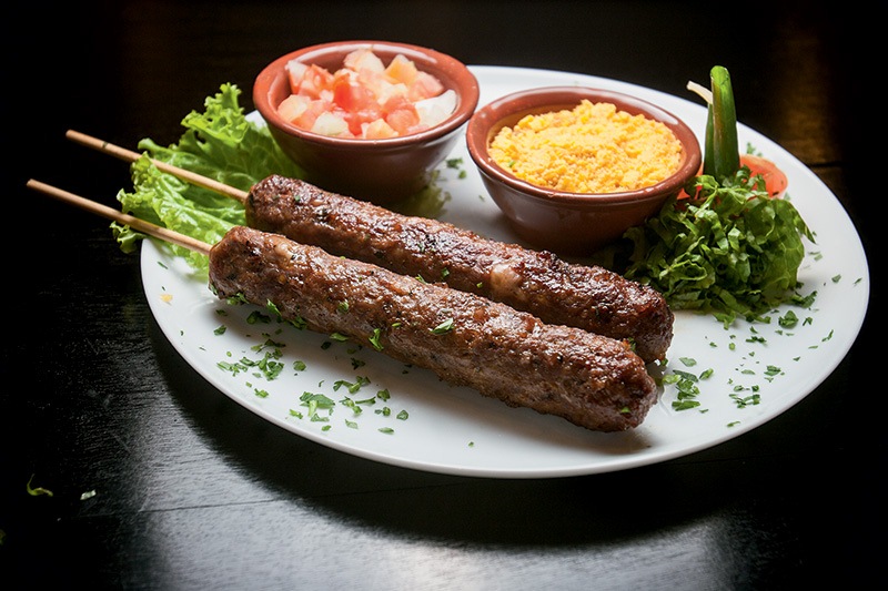 O espetinho de cafta acompanhado por vinagrete e farofa O espetinho de cafta acompanhado por vinagrete e farofa