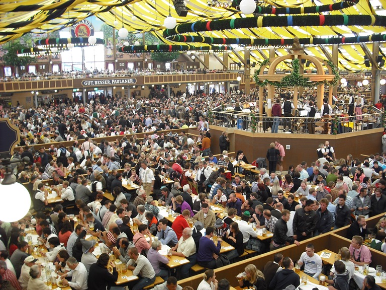 oktoberfest-munique Vista de cinema, tenda com muitas mesa e bancos repletos de pessoas