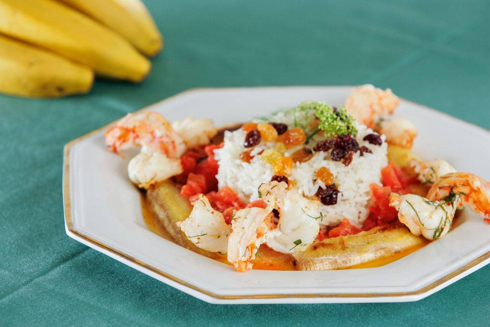 Camarão com tomate e banana flambado em aguardente da fruta ao lado de arroz com passas Camarão com tomate e banana flambado em aguardente da fruta ao lado de arroz com passas