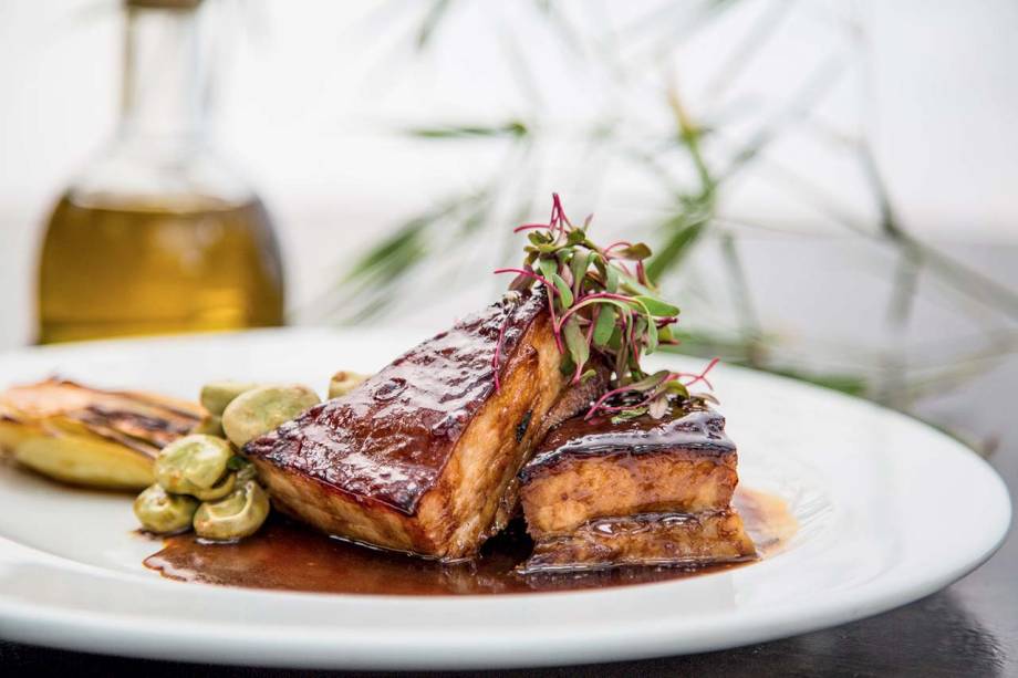 A tenra barriga de porco de pele crocante vem com acelga bok choy, favas e molho de tangerina