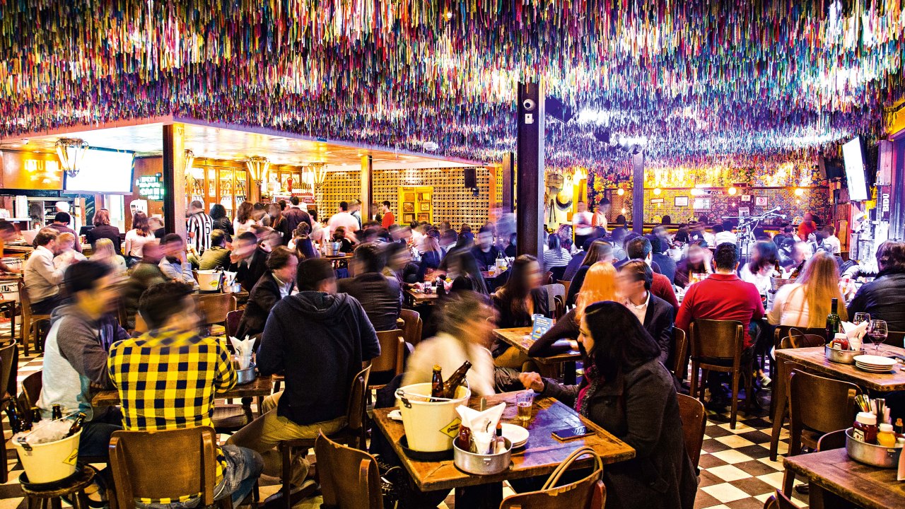 Ambiente de bar repleto de fitinhas no teto com pessoas sentadas