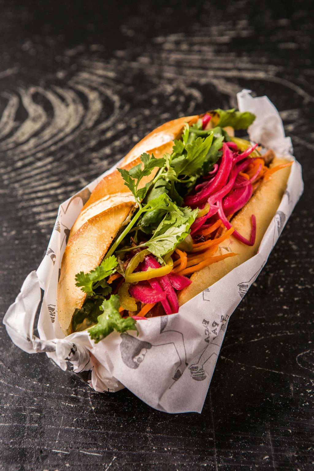 O lanche vietnamita traz na baguete frango levemente agridoce, cenoura, maionese de shoyu, coentro, pimenta jalapeño e picles O lanche vietnamita traz na baguete frango levemente agridoce, cenoura, maionese de shoyu, coentro, pimenta jalapeño e picles