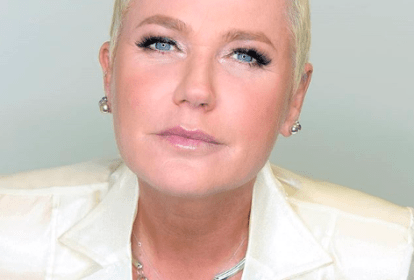 Imagem mostra Xuxa de terno e colar, olhando séria para a câmera