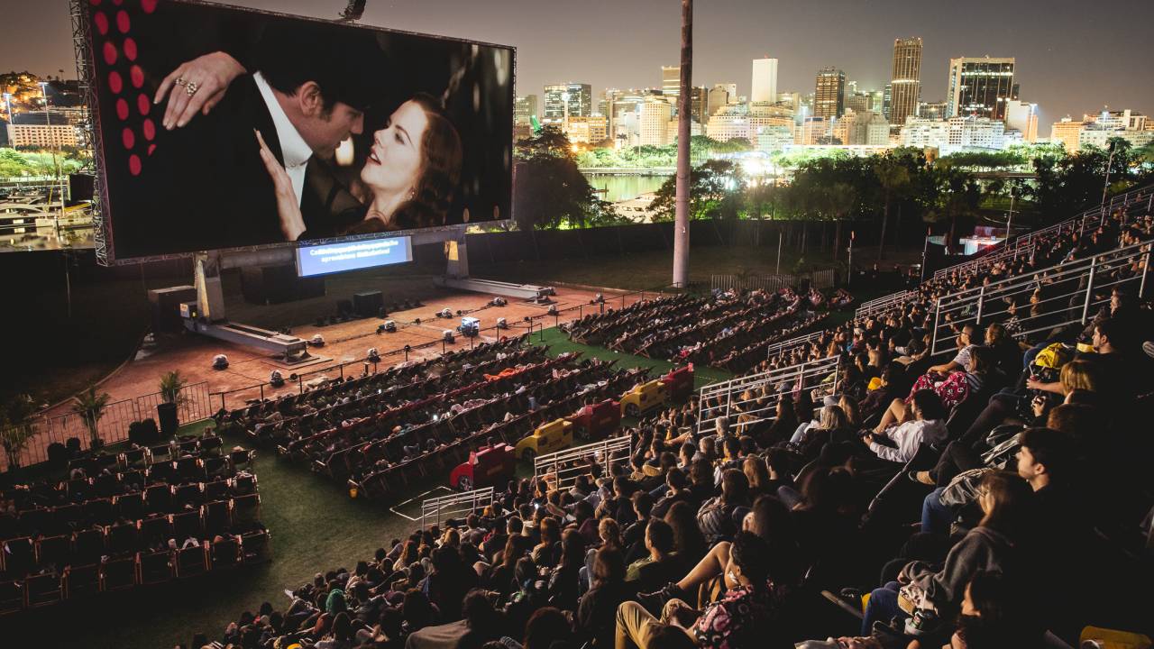 Evento Open Air, no Jockey Club: foto exibe telão ao ar livre e plateia em arquibancada.