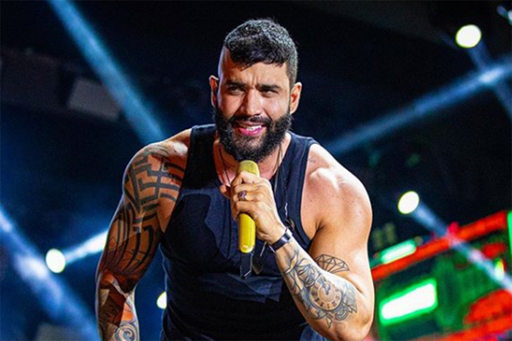Imagem mostra Gusttavo Lima com microfone na mão, em palco, durante show