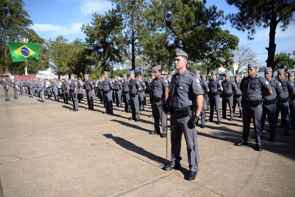Fileira de policiais posa para foto em local aberto. Um deles se posiciona de pé à frente de todos.