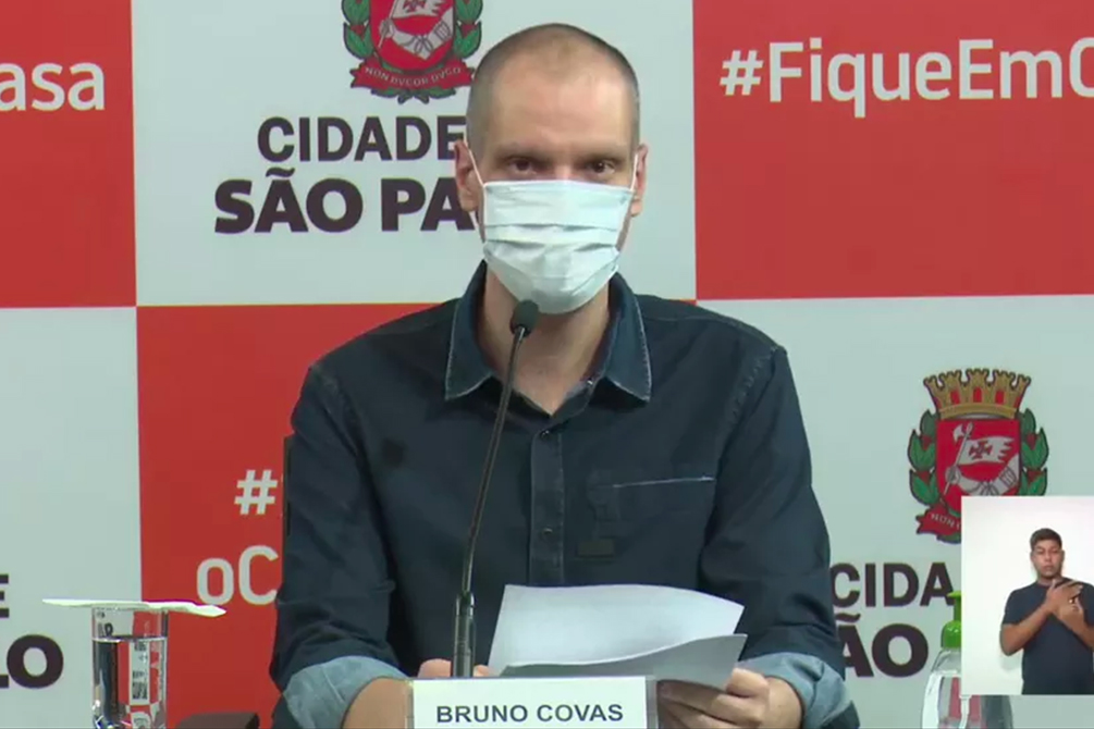 O prefeito Bruno Covas aparece em coletiva de imprensa usando máscara diante de microfone