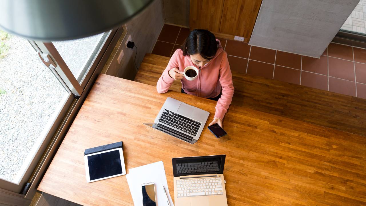 Imagem mostra mulher sentada em mesa diante de computador, trabalhando em regime de home office