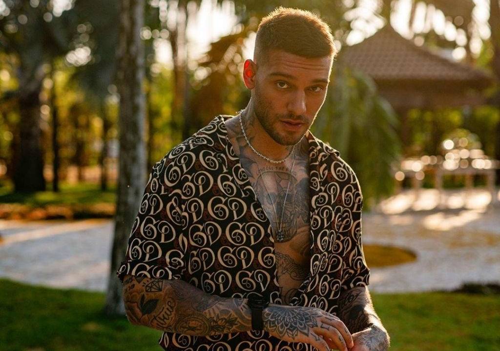 lucas lucco sob a luz do sol olhando para a câmera com a cabeça semiabaixada