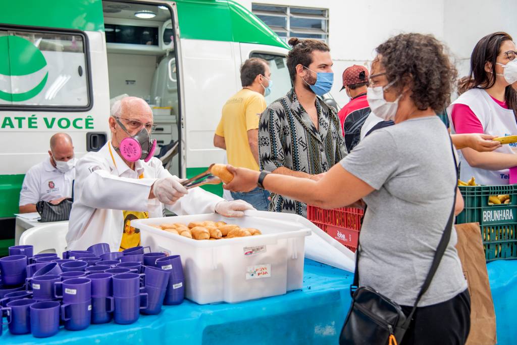 Padre Júlio Lancelotti Padre Júlio Lancellotti, de máscara, distribuindo pão com pinça de uma caixa de plástico branca com pães.