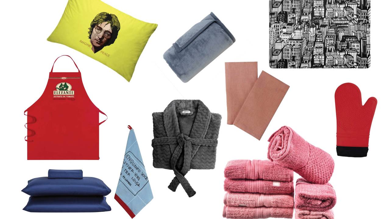 Seleção de itens de cama, mesa e banho, incluindo fronha amarela com rosto de John Lennon, lençóis azul-marinho, roupão cinza e avental de cozinha vermelho com estampa do personagem Jotalhão.