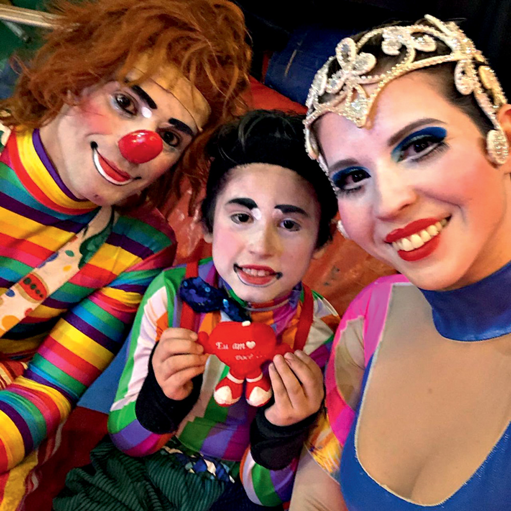 Circenses Ícaro sorri com os pais, Rejane e Giovanni. Todos estão maquiados e com roupas de circo