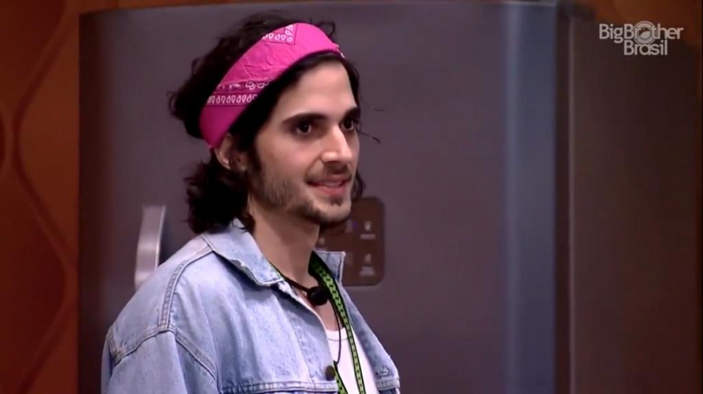 Fiuk, usando uma faixa rosa para prender o cabelo. Ele está na casa do BBB21, a imagem vem de uma das câmeras da casa.