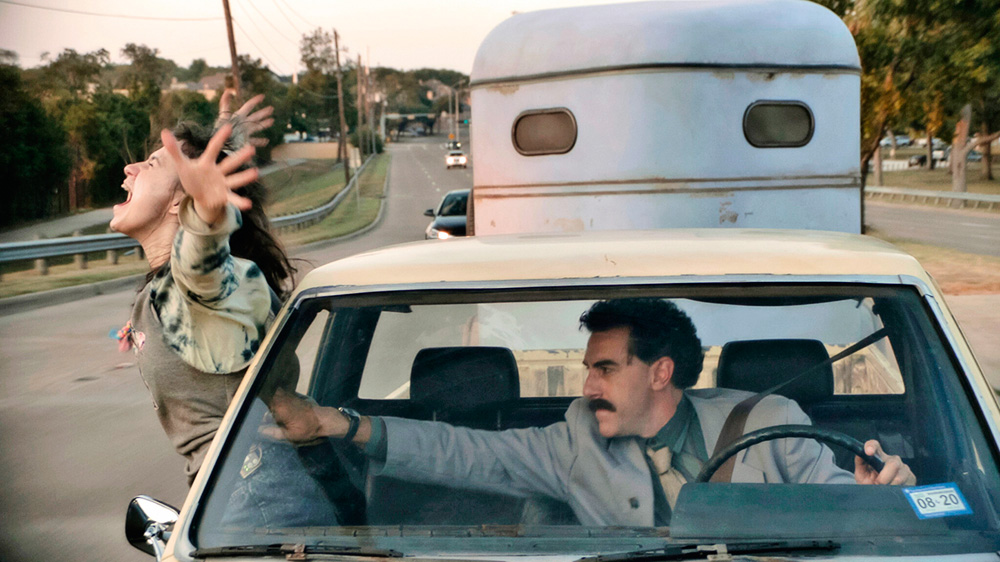 borat.jpg Borat dentro do carro, segurando a filha que está saindo pela janela