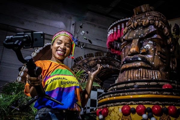 visita-barracao-escola-de-samba-carnaval-2021-airbnb menina em barracão de escola de samba segura celular com pau de selfie