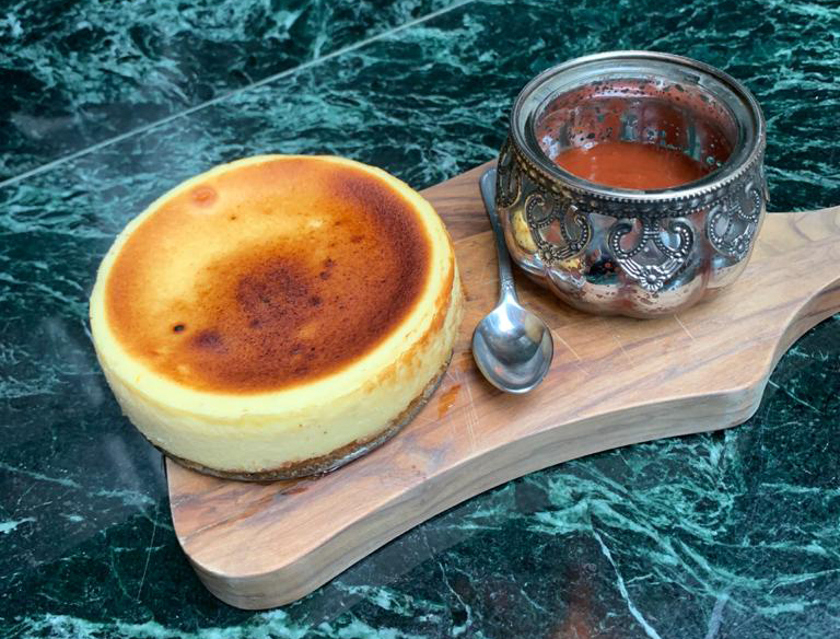 Bodega La Barra Sobre uma tábua, repousa uma torta de queijo redonda e uma vasilha com molho de goiabada mais uma colher