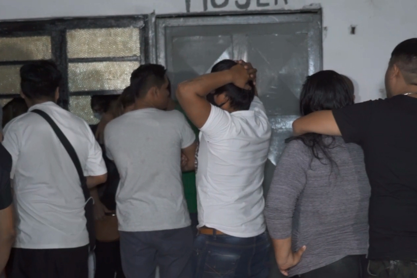 Imagem mostra pessoas aglomeradas, de costas, perto de parede de evento clandestino