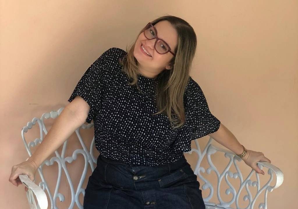 Imagem de Ana Lúcia sorrindo, sentada em um banco branco