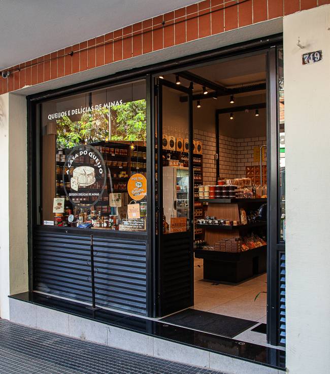 Fachada da loja A Casa do Queijo. Porta à esquerda com vitrine de vidro sobre estrutura metálica preta à esquerda.