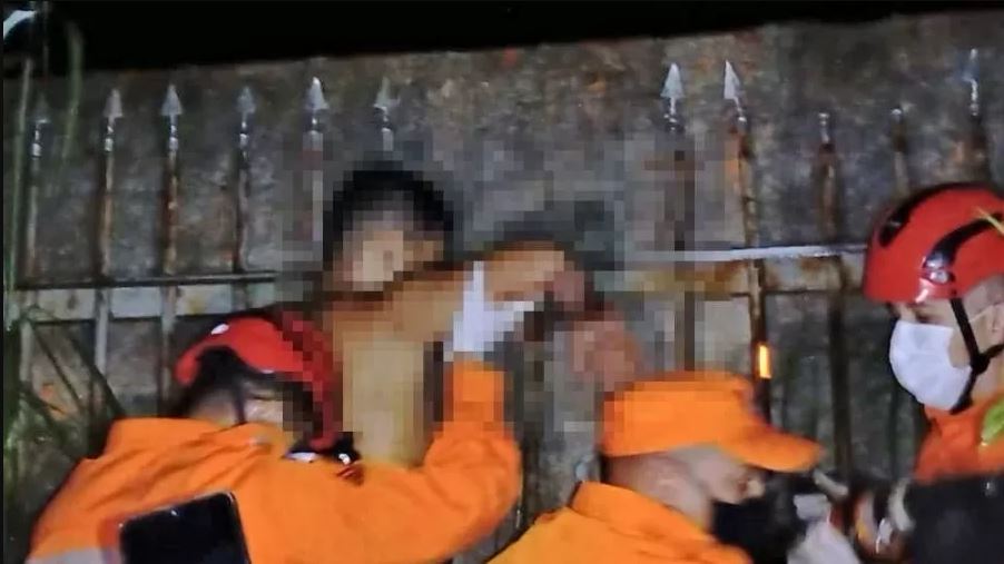 Imagem mostra bombeiro ajudando jovem a retirar o braço da lança do portão; imagem está pixelada