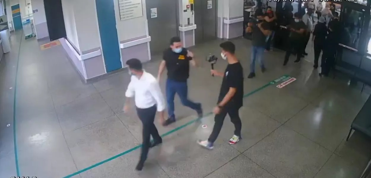 Imagens de câmera de segurança mostram momento da invasão feita por Kim Kataguiri e Mamãe Falei em hospital de Guarulhos. Na imagem, três homens andam por um corredor largo.