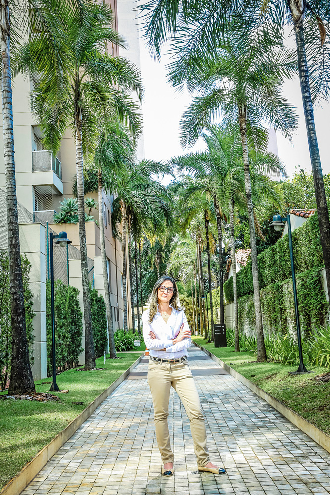 São Paulo 12 abril 2021Ligia Ramos VolpiFoto Alexandre Battibugli VSP Ligia, em um corredor arborizado em um dos condomínio. Ela está de pé e há palmeiras em volta.