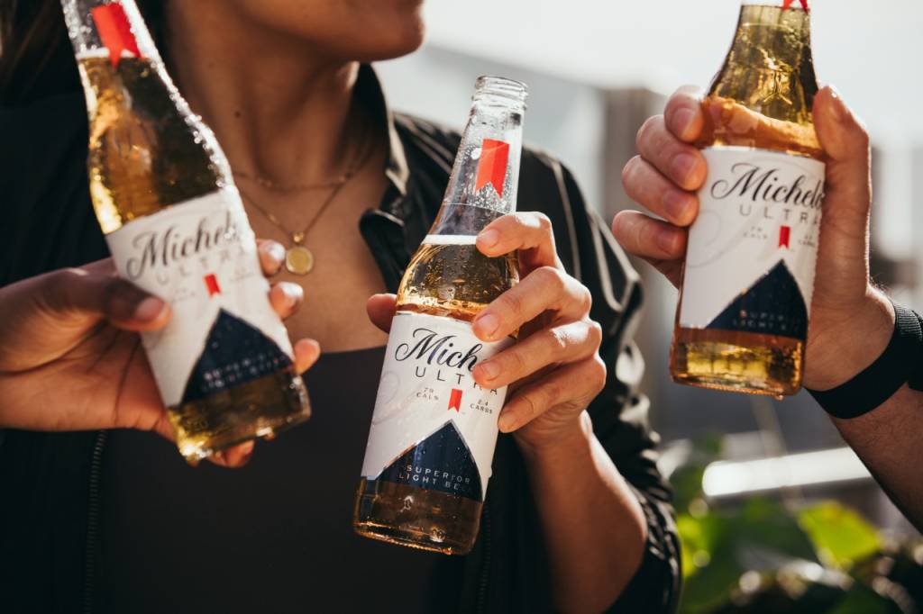 Michelob Ultra Três pessoas seguram garrafas da cerveja Michelob Ultra, onde o foco da imagem são apenas as mãos e as cervejas