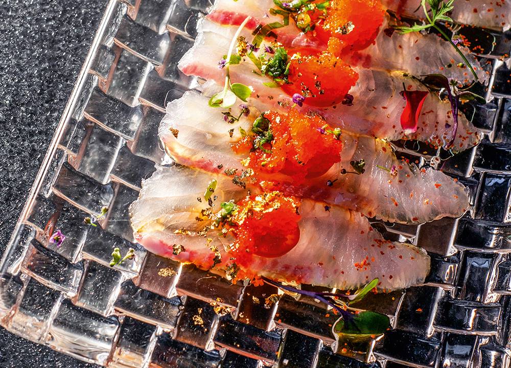 Prato retangular de cristal com sashimis coberto por ovas de peixe e pimenta.