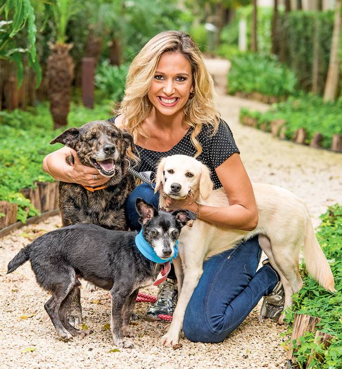 Luisa Mell, ativista e apresentadora de TV, posa de joelhos abraçada com três cachorros.